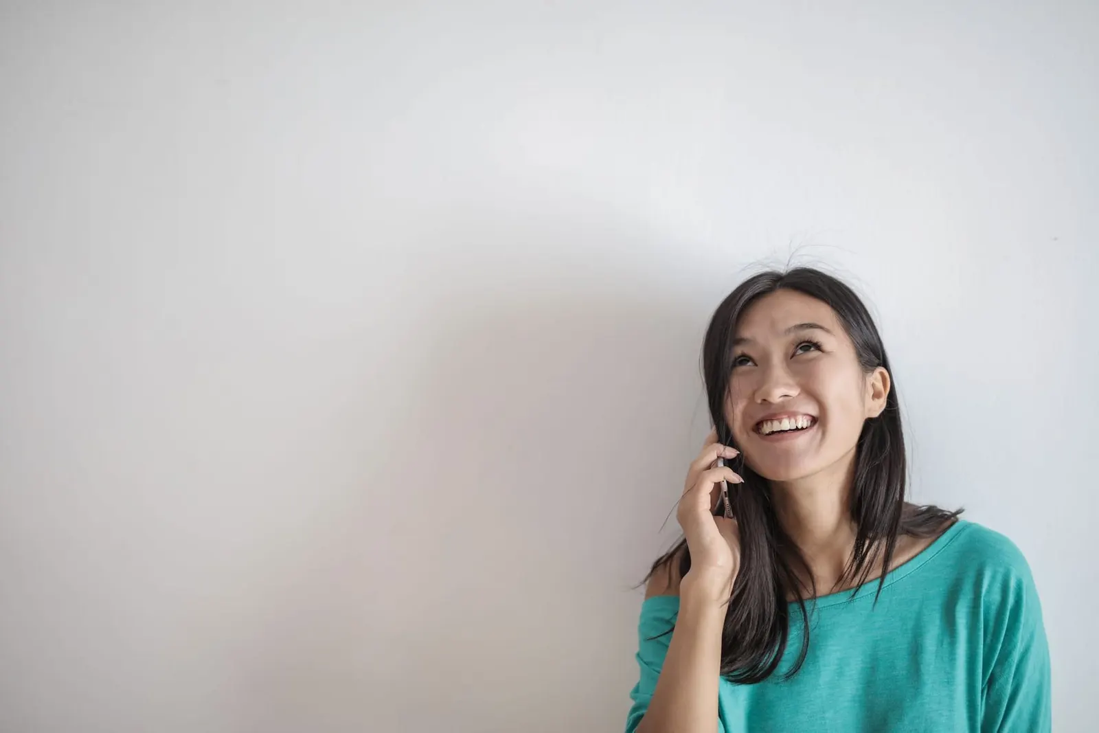 A smiling woman talking on her phone against a white wall